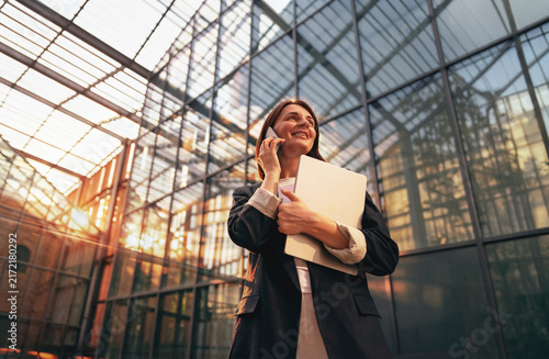 Businesswoman on a phone call at a glass atrium at sunset