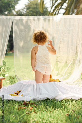 Curly-Haired Toddler Standing in Outdoor Bathtub and Looking at the Garden
