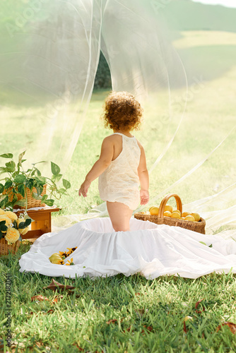 Curly-Haired Toddler Standing in Outdoor Bathtub and Looking at the Garden