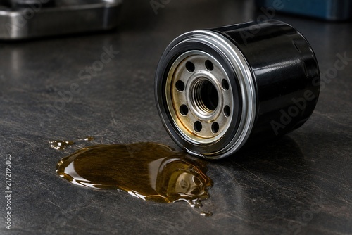 Used automotive oil filter beside spilled engine lubricant on a dark workshop bench