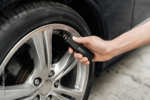 Driver checking car tire pressure with digital gauge during routine vehicle maintenance