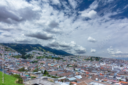 Panoramic view of the historic downtown center of Quito, Ecuador, featuring colonial architecture, dense cityscape, and the iconic Basilica del Voto Nacional under dramatic clouds.
