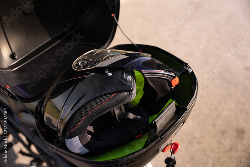 Black helmet rests in open motorcycle storage compartment. Green interior lining adds contrast to sleek exterior. Compact design fits snugly inside bike's rear compartment. Ideal for travel, commuting