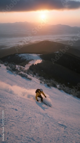 A snowboarder gracefully glides down a snowy slope as the sun sets behind distant peaks, casting warm hues across the tranquil winter scenery