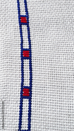 Close-up of white embroidered fabric with blue stitching and red details