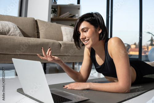 Young woman doing online fitness class on yoga mat at home