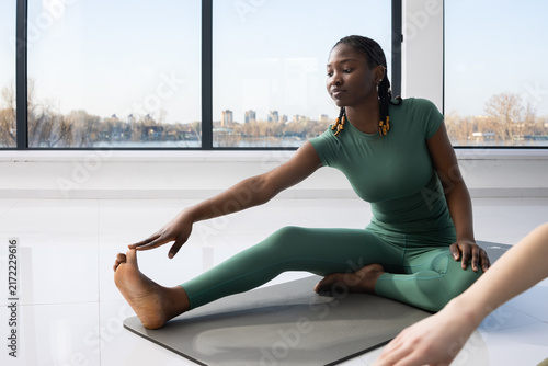 Woman in green activewear stretching her leg on a yoga mat indoors