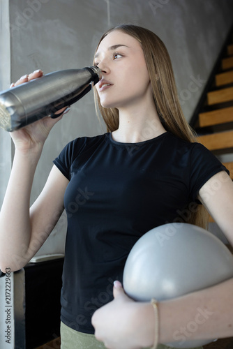 Young woman in activewear drinks water from a metal bottle after exercise