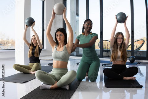 Diverse group of women practicing yoga with small exercise balls in a bright studio