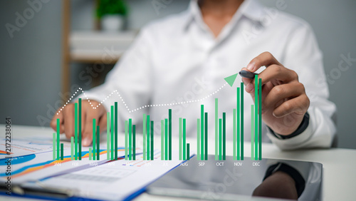 Businessman hand drawing virtual financial growth bar chart and arrow graph with pen on table, business stock market investment, financial planning, development and progress concept.