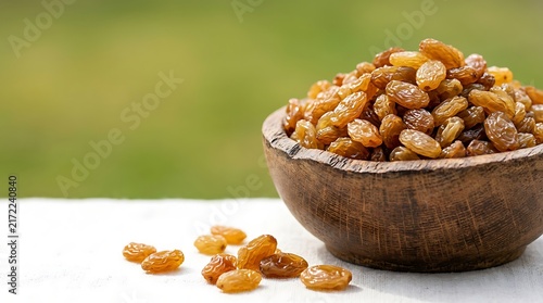 A small rustic wooden bowl filled with delicious golden raisins on a white table outdoors