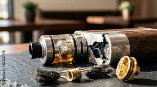 Broken vape mod device with cracked glass tank and leaking liquid. Damaged electronic cigarette on slate surface