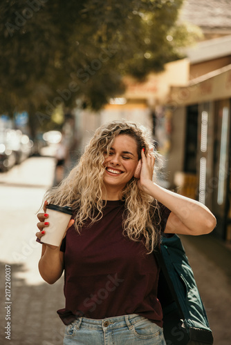 Happy woman enjoying music and coffee on city street
