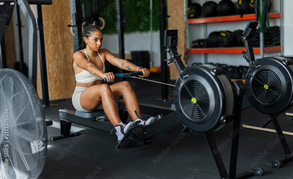 Fototapeta premium Young woman training core body on rowing machine