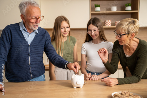 Fotografía Happy grandparents saving money with their granddaughters using a white piggy ba