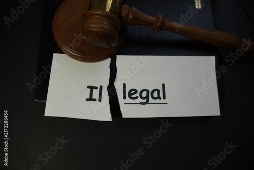 Wooden judge gavel resting above a torn paper with the word illegal
