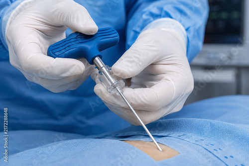 Macro close-up of a hematologist's hands in sterile gloves holding a specialized bone marrow biopsy needle handle, positioning it for pelvic bone aspiration