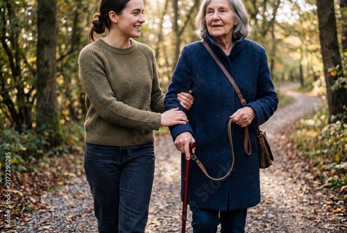 Young woman providing supportive care by walking slowly with her elderly mother along a quiet forest trail during a serene autumn day