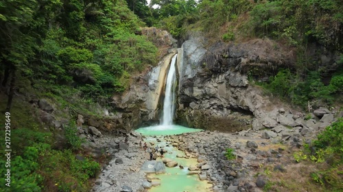 Aerial drone approaching Mangku Sakti waterfall above turquoise river gorge Sembalun Lombok