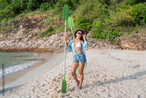 Photography A portrait of a woman standing on the beach, holding a paddle board paddle by th