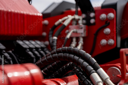 High-pressure hydraulic hoses with black protective spiral wrap and metal fittings connected to red heavy machinery.