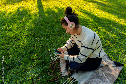 Картината върху платно Woman enjoying music in park, using smartphone and wearing headphones, relaxing