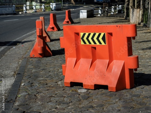 A row of orange plastic traffic barriers with chevron directional signs lined up along a paved street side.