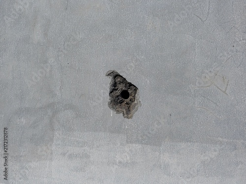 Abstract background texture of a gray cement wall featuring a damaged chipped hole in the middle.