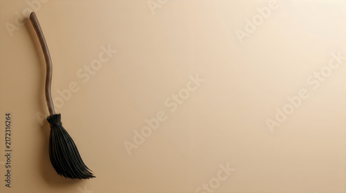 A vintage witch's broom leaning against a plain beige wall in a simple setting