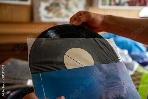 Male hand pulling a black vinyl record out of an inner paper and plastic sleeve, illustrating vintage music listening, audio collecting, and analog sound hobby.