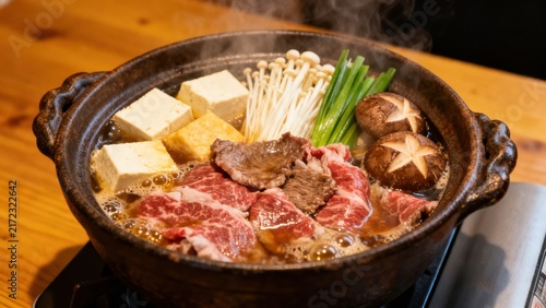 A bubbling hot pot of Japanese sukiyaki featuring thinly sliced marbled beef, tofu, shirataki noodles, Napa cabbage, enoki mushrooms, and shiitake, simmered in a sweet-savory soy-based broth, ready fo