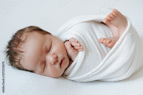 A newborn baby is sleeping in a diaper against a white, isolated background; space for text. The little baby is sleeping sweetly.