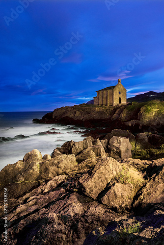 Santa Katalina chapel standing on a rocky cliff over the ocean under a dramatic cloudy sky in Mundaka Basque Country Spain