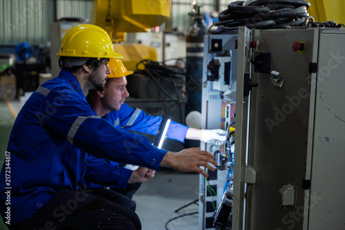 Obraz na plátně Industrial technician and engineer use an inspection light and tablet to examine a machine control cabinet in a factory