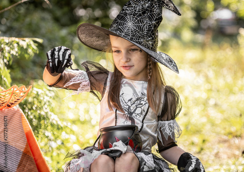 Bild auf Leinwand Girl Dressed as a Witch Examines a Small Object During Halloween Festivities in
