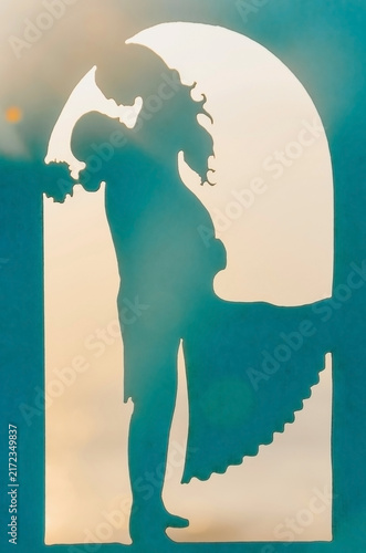 wedding paper decor. Couple stands in  romantic pose under an arch silhouette at sunset near the beach. background shows soft colors of  sunset over the ocean. scene reflects  moment of joy connection