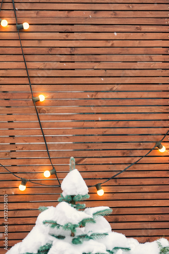 Rustic wooden backdrop with glowing lights, evergreen branches and snow