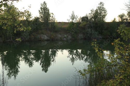 Tranquil evening landscape of a flooded quarry lake surrounded by dense reeds and green trees at dusk