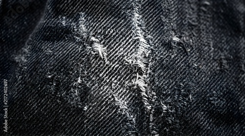 Distressed black denim fabric texture with frayed edges and worn detail