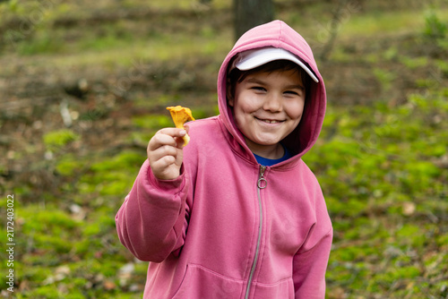 Enthusiastic smiling little child with chanterelle mushroom in his hand. Focus on the boy. Boy showing edible mushroom he found in the forest. Weekend fun family activity.
