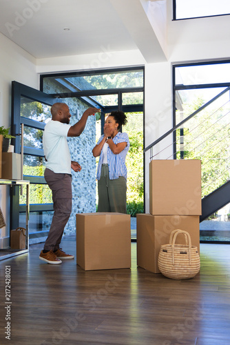 African American couple standing in entryway holding keys amid packed moving boxes and basket