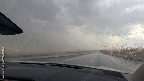 Car drives through heavy rain front view as windshield wipers clear water under dark storm clouds, showing hazardous road conditions, weather travel risk, vehicle safety, and severe storm driving