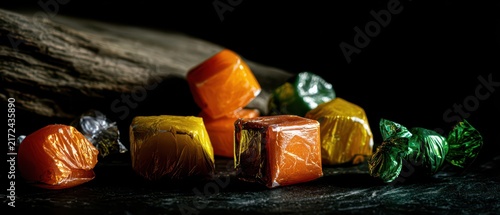 Mixed halloween foil wrapped round and square candies in orange yellow green on a dark wooden background for seasonal poster and product display