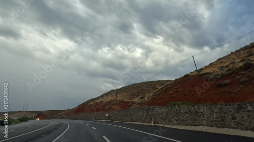Car traveling on a curving highway in wide view beneath heavy storm clouds in Turkey, showing changing road conditions, regional transport, route planning, travel safety, and long-distance mobility