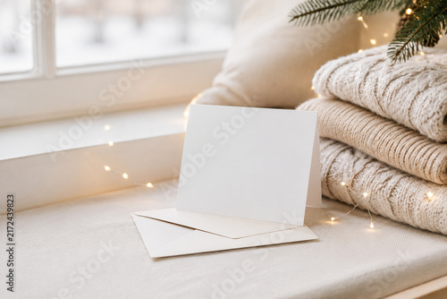 Blank card with envelope, string lights and folded sweaters on window seat, holiday card inspiration