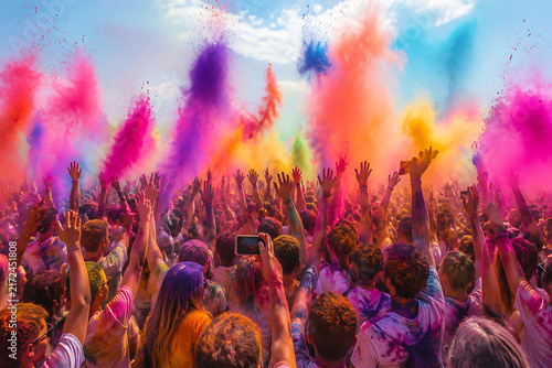 Massive Crowd Raising Hands Under Explosive Sky of Multi Color Powder Clouds During Outdoor Holi Festival Celebration Event under Bright Blue Sunny Sky