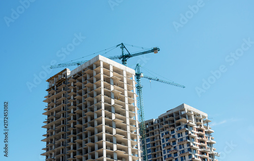 Detailed view of reinforced concrete building frames and heavy tower cranes working on site. Industrial background showcasing civil engineering, high-rise construction technology, and safety