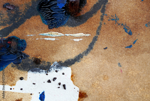Close-up abstract photograph of colorful paint marks, brush strokes, splashes, and textured pigments on brown paper.