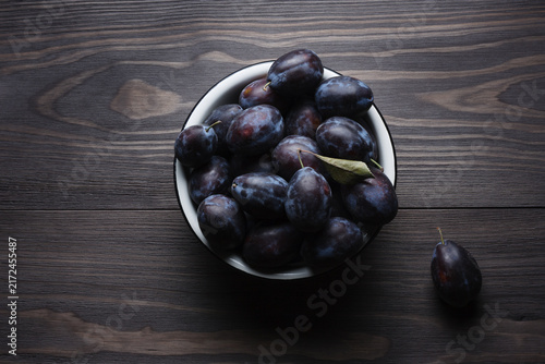 Ripe fresh plums in enamel bowl on wooden table