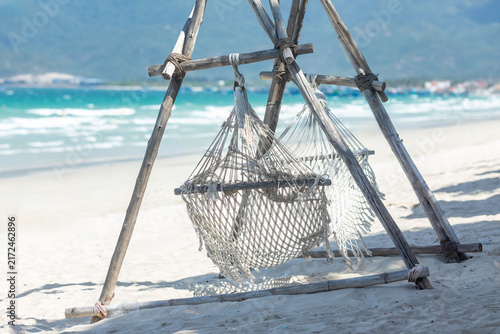 Foto Hammock made of netting is suspended between wooden posts on a sandy beach, with turquoise ocean waves gently lapping at the shore and distant mountains